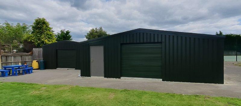 Wide view of a forest green steel building with a roller shutter door and a grey personal access door.