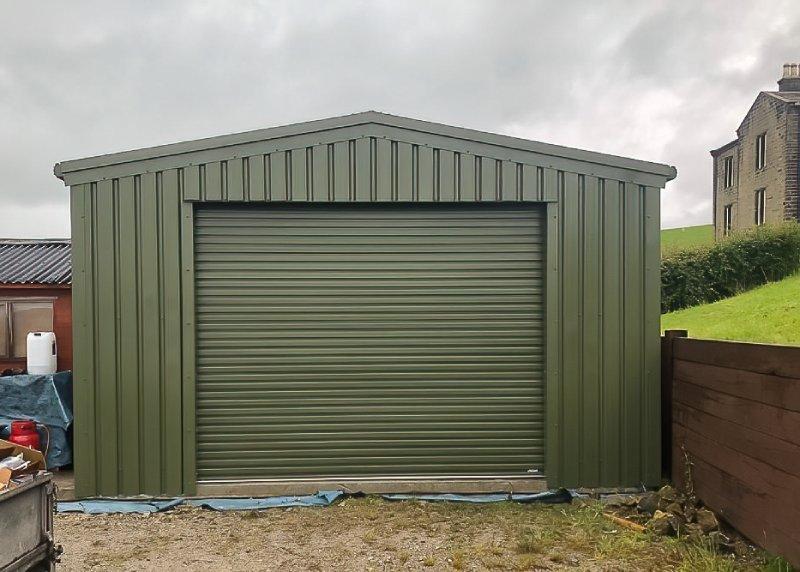 Direct front view of a compact olive green steel garage with a single wide roller shutter door and a pitched roof.